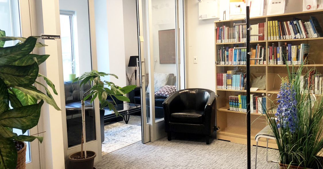 The entrance area of the TCDC and EdTech offices. There is a bookcase filled with books with a black chair in front of it. There are plants in the foreground.