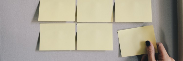 Photo of a hand holding a post-it note and sticking it next to a group of other post-it notes.