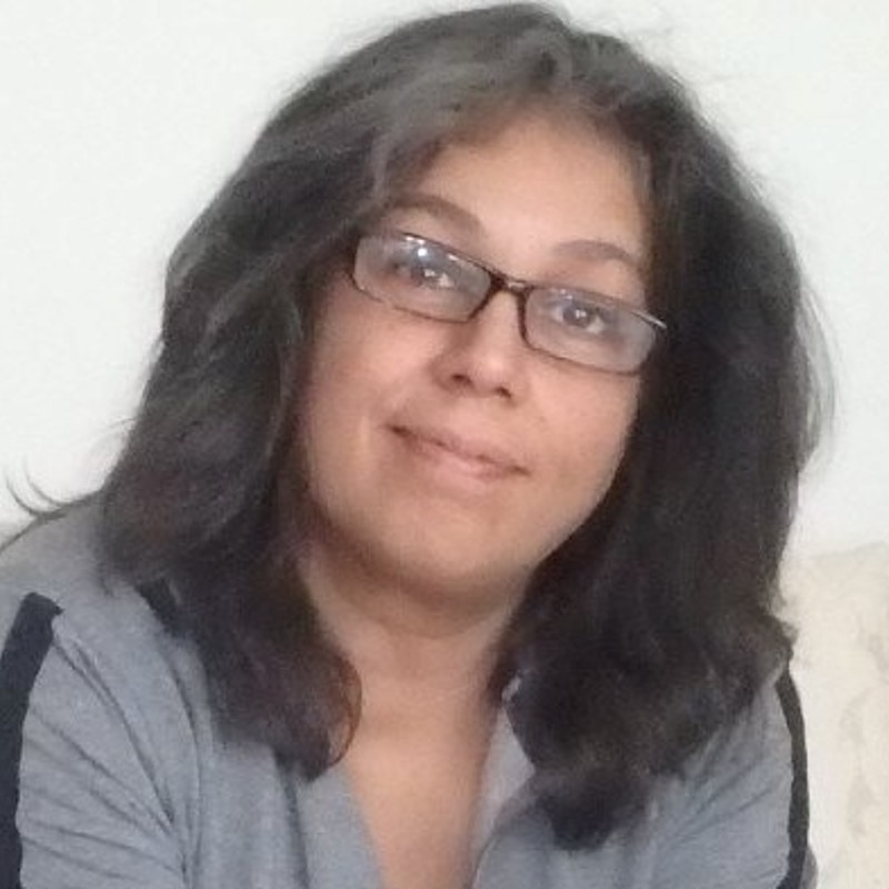 Gitanjali with medium length dark hair. She is wearing glasses and a grey shirt.