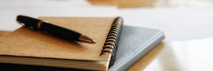 A pen placed on top of a stack of notebooks.