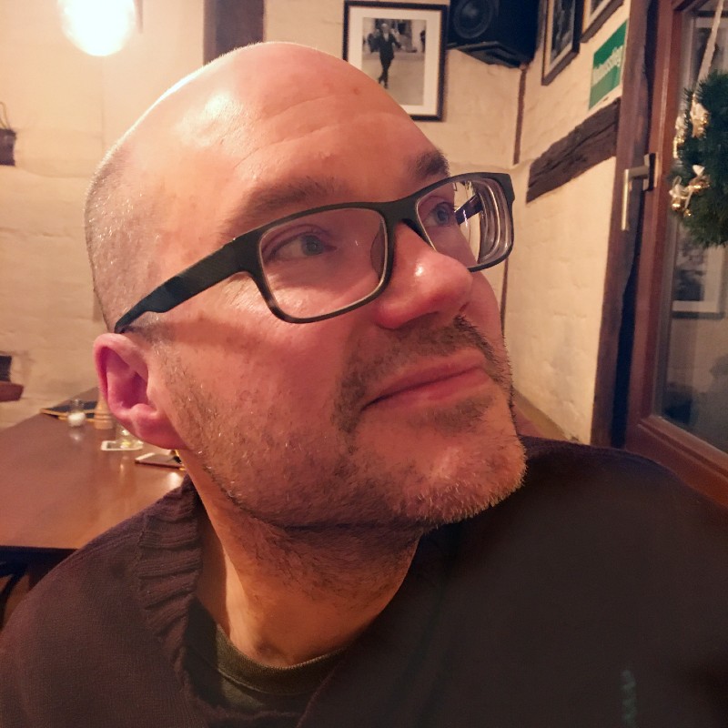 James in a restaurant, wearing glasses and looking up and over to the right side.
