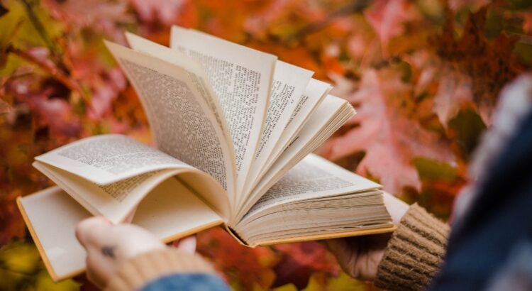 An open book with the pages being flipped, in the background are fall leaves.