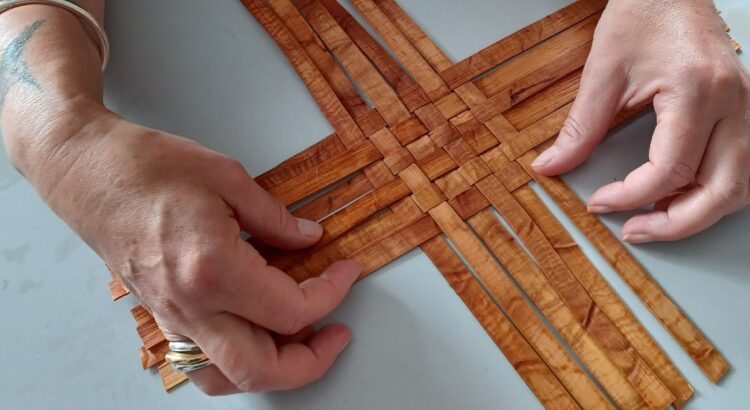Close-up of hands weaving a basket with thin strips of cedar.